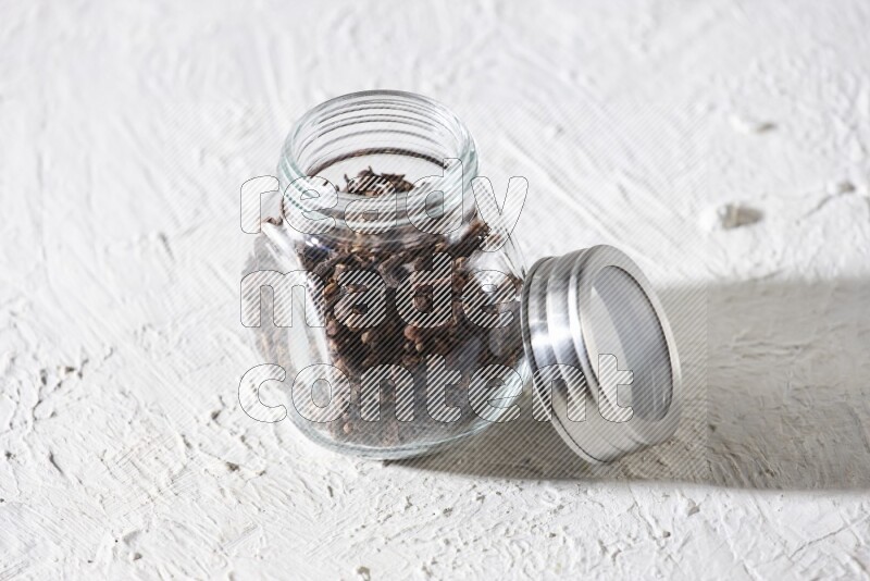 A glass spice jar full of cloves on textured white flooring
