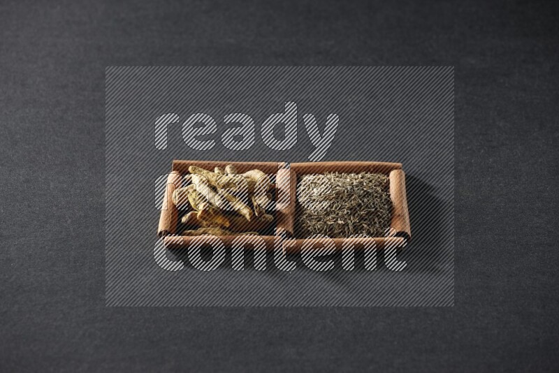 مربعان من أعواد القرفة ممتلئان بحبوب الكمون وأصابع الكركم علي خلفية سوداء