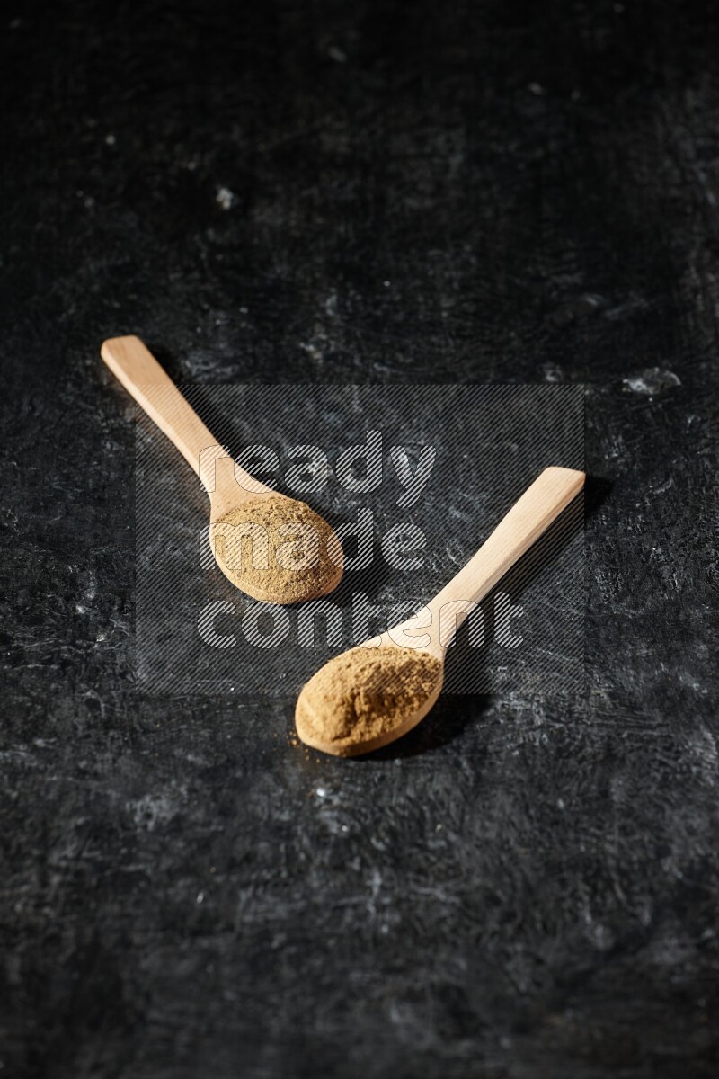Wooden spoons full of allspice powder on a textured black flooring