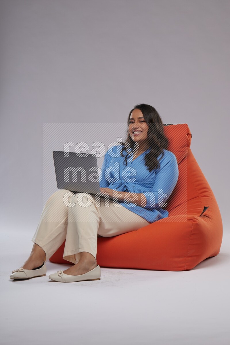 A woman sitting on an orange beanbag and working on laptop