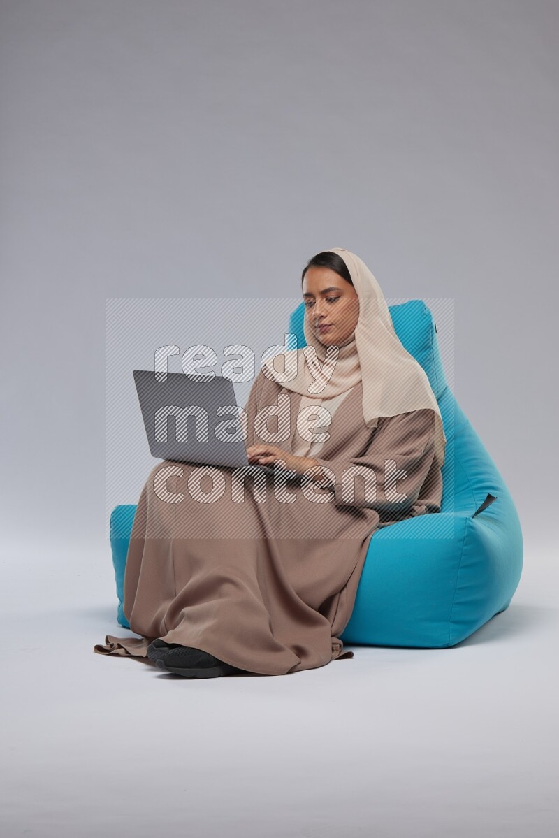 A Saudi woman sitting on a blue beanbag and working on laptop