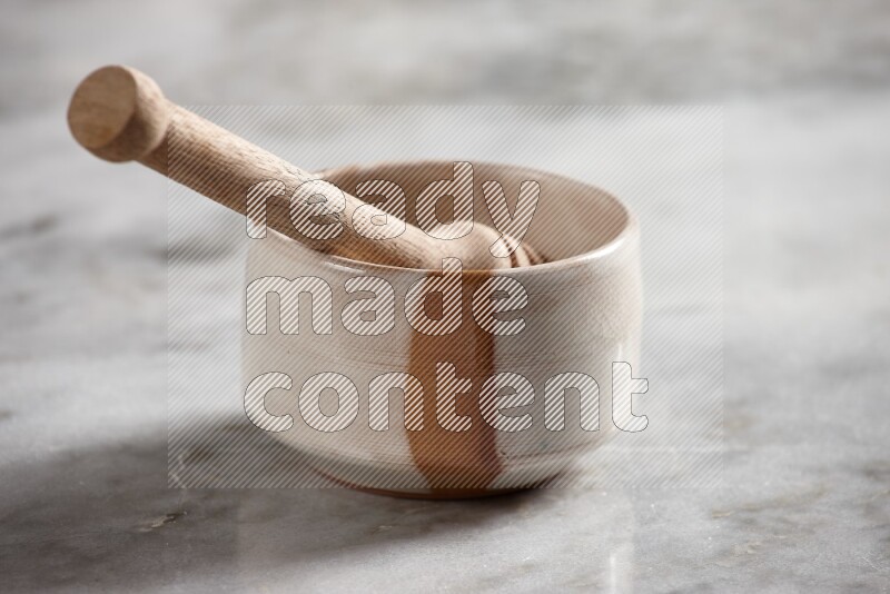 Multicolored pottery bowl with wooden honey dipper in it on grey marble background