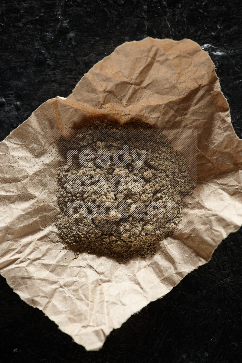 Cardamom powder in a crumpled piece of paper on textured black flooring