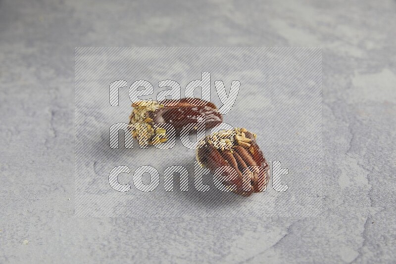 Two pecan stuffed dates covered with Dark chocolate and chopped pistachios on alight grey background