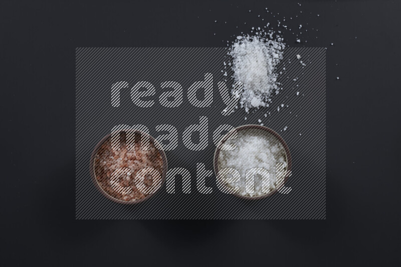 2 pottery bowls one is filled with himalayan salt and the other with white salt on black background