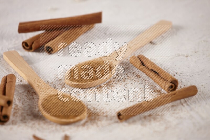 Two wooden spoons full of cinnamon powder with cinnamon sticks on white background