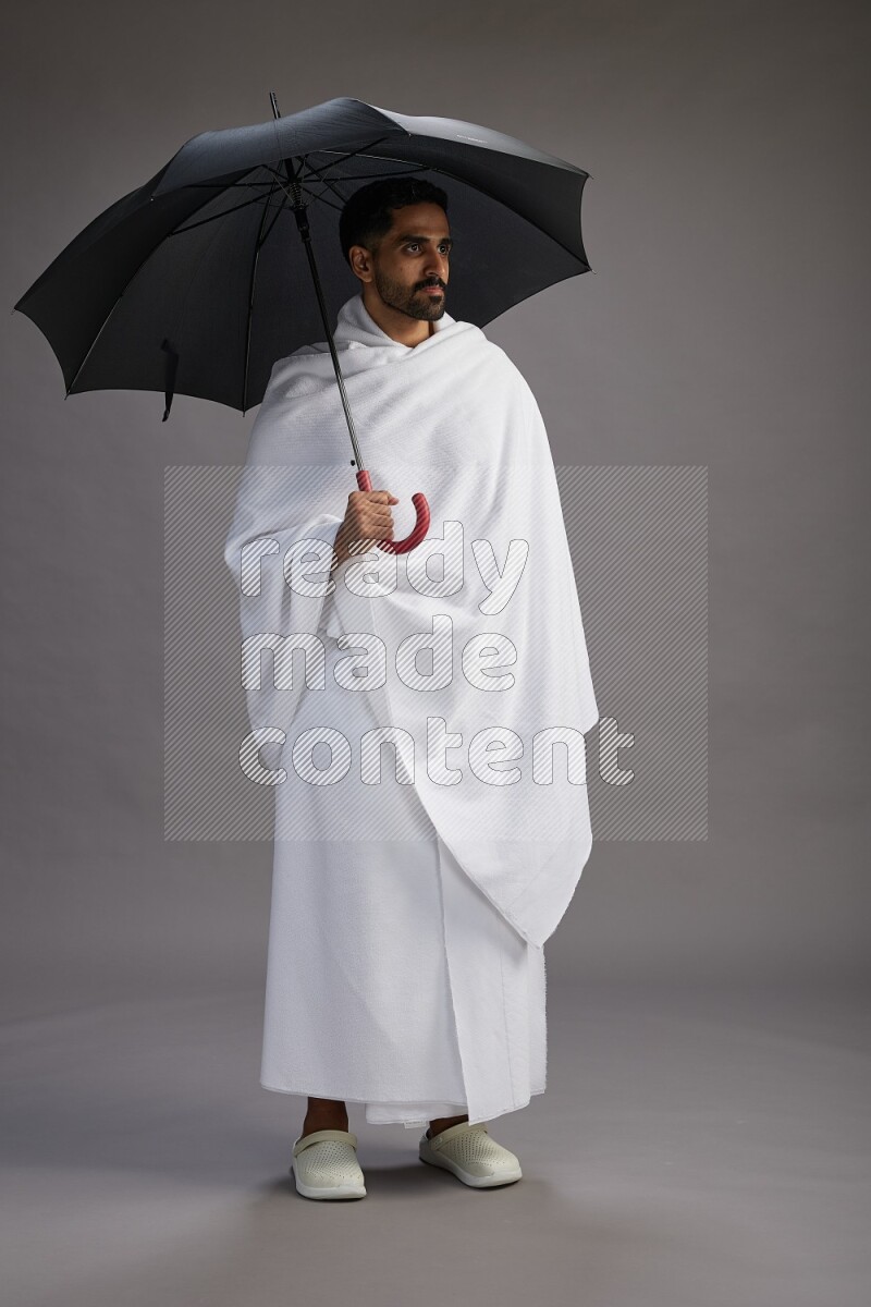 A man wearing Ehram Standing holding umbrella on gray background