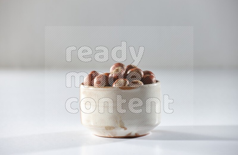 A beige ceramic bowl full of hazelnuts on a white background in different angles