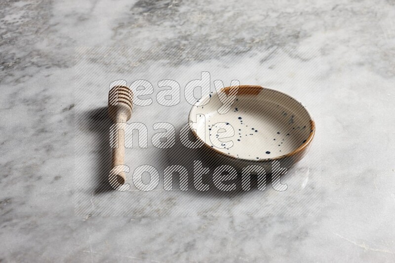 Multicolored pottery bowl with wooden honey dipper on the side on grey marble background