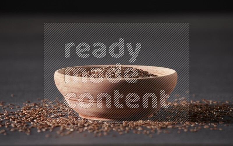 A wooden bowl full of flax surrounded by the seeds on a black flooring in different angles
