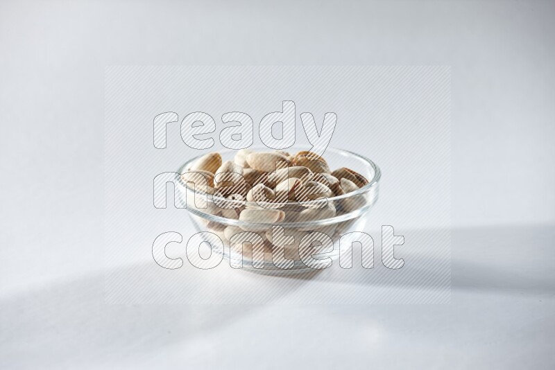 A glass bowl full of pistachios on a white background in different angles