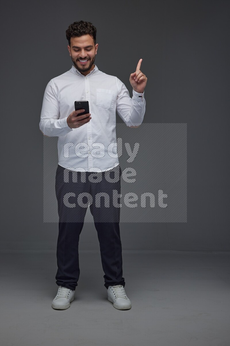 A man wearing smart casual standing and using his phone and making multi hand gestures eye level on a gray background