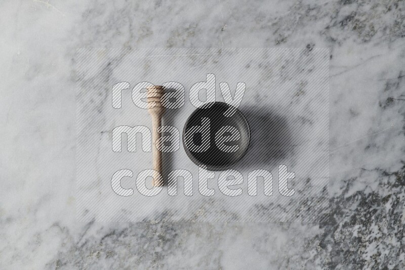 Black pottery bowl with wooden honey dipper on the side on grey marble background