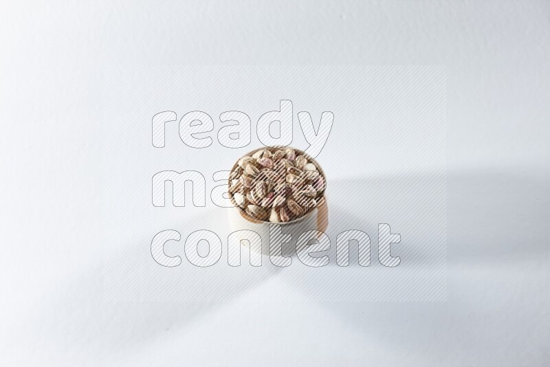 A beige ceramic bowl full of peeled pistachios on a white background in different angles