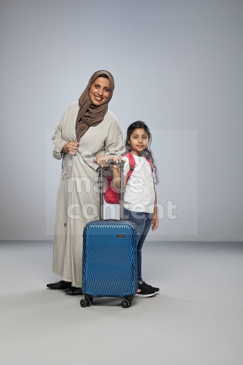 Mom and daughter standing pulling a carry-on bag on gray background