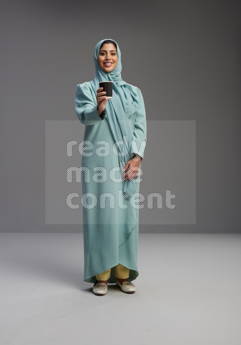 Saudi Woman wearing Abaya standing  holding paper cup on Gray background