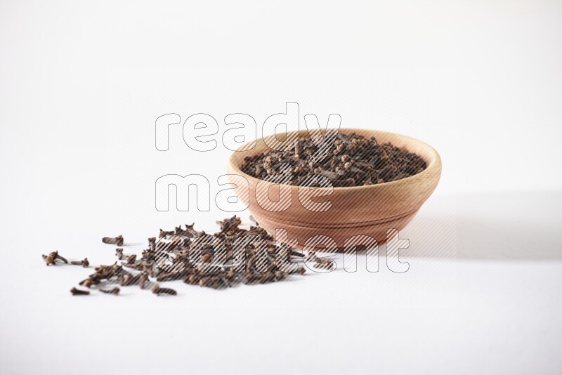 A wooden bowl full of cloves with spread grains on a white flooring