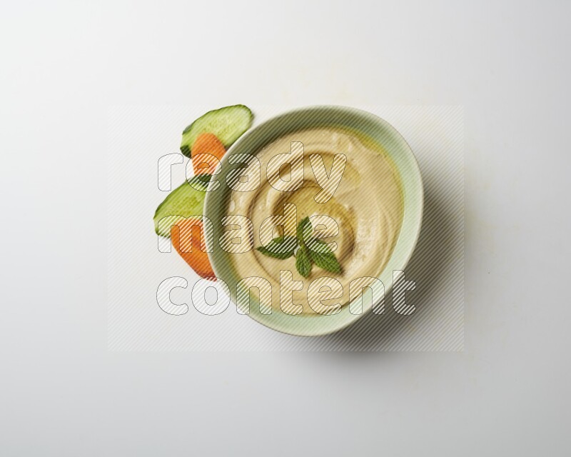 Hummus in a green plate garnished with mint on a white background