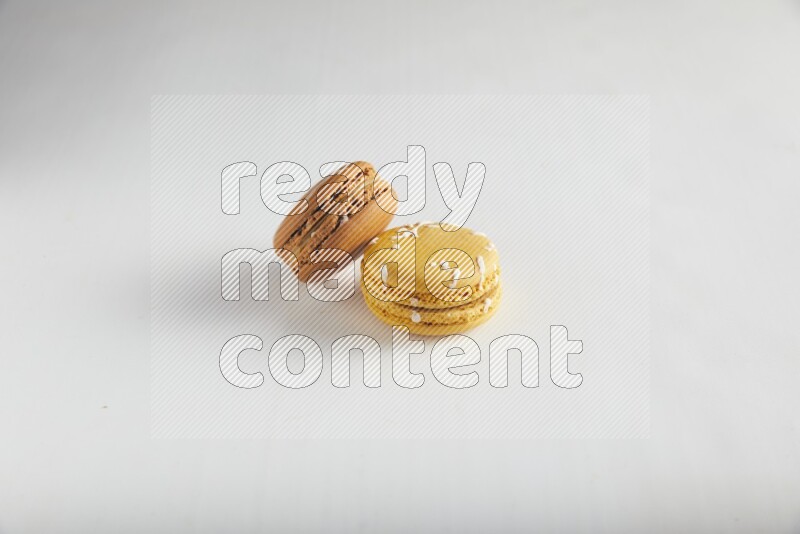 45º Shot of of two assorted Brown Irish Cream, and Yellow Piña Colada macarons on white background