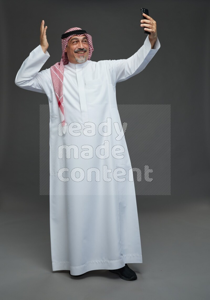 Saudi man with shomag Standing taking selfie on gray background