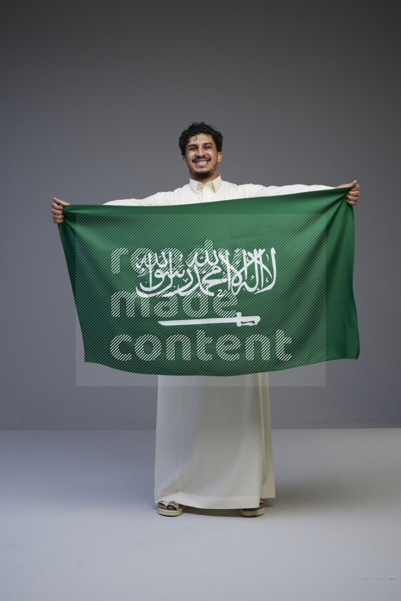 رجل سعودي يرتدي ثوب ابيض ويحمل العلم السعودي