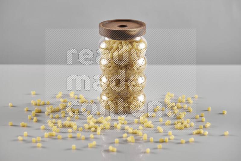 Raw pasta in a glass jar on light grey background