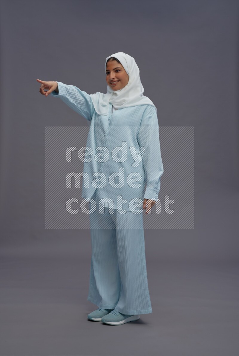 Saudi woman wearing hijab clothes standing interacting with the camera on gray background