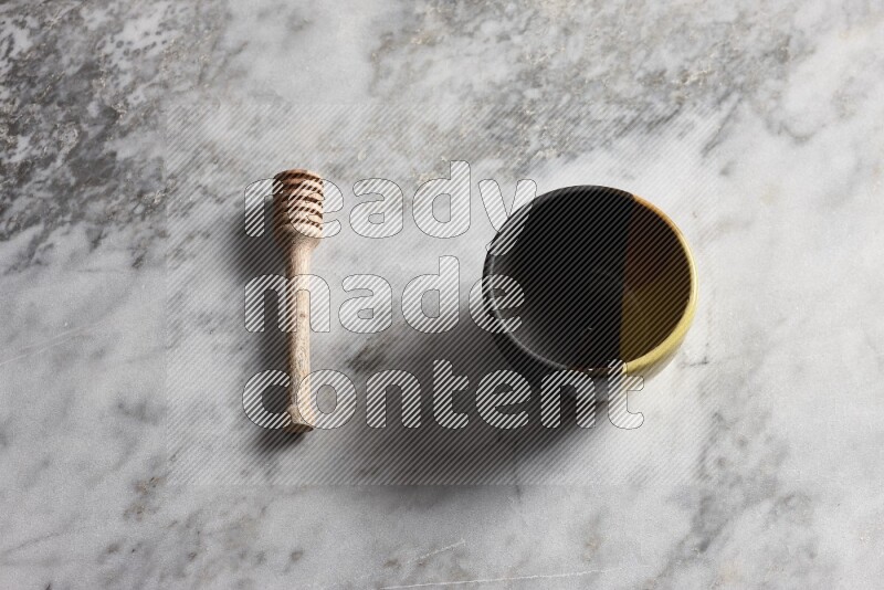 Multicolored pottery bowl with wooden honey dipper on the side on grey marble background