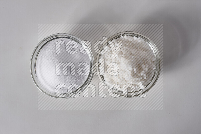 2 glass bowls one is filled with table salt and the other with coarse sea salt on white background