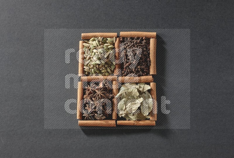 4 squares of cinnamon sticks full of star anise, cardamom, cloves and bay laurel leaves on black flooring