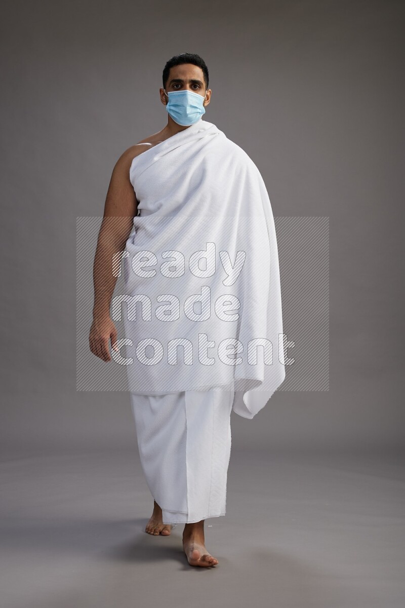 A man wearing Ehram with face mask Standing Interacting with the camera on gray background
