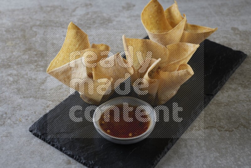 wonton cups with soy sauce ramkin on rectangle slate on grey textured counter top