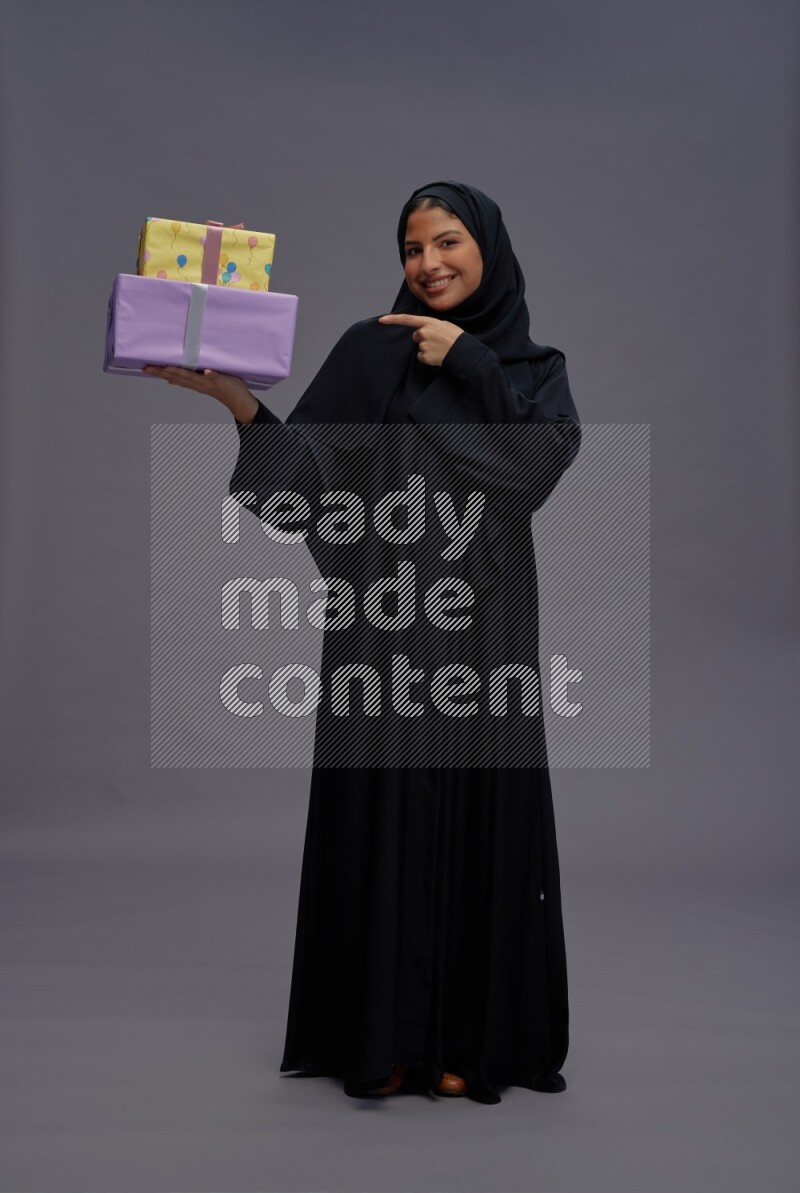 Saudi woman wearing Abaya standing holding gift box on gray background