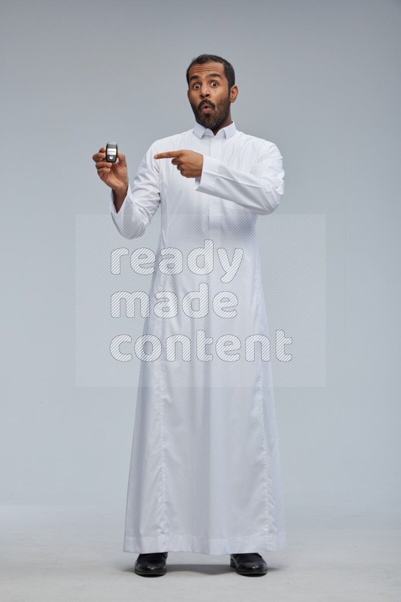 Saudi man wearing thob and shomag standing holding car key on gray background