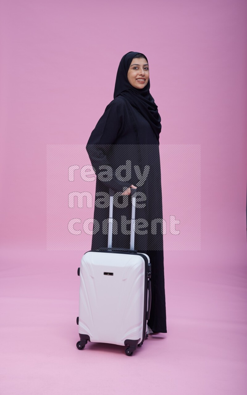 Saudi woman wearing Abaya standing holding bag on pink background