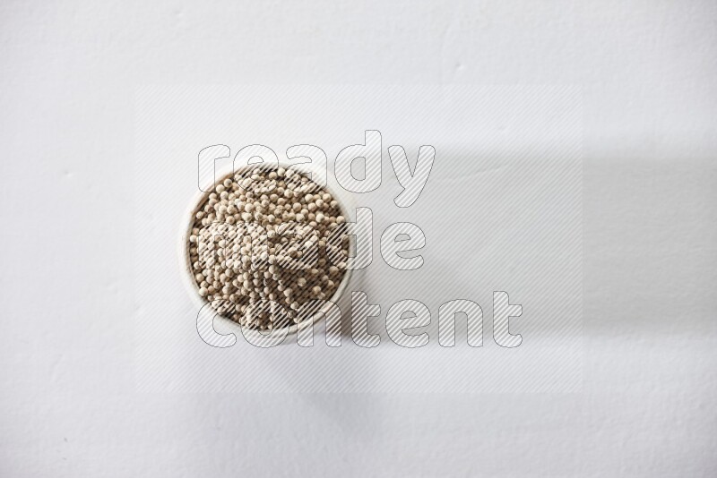 A beige pottery bowl full of white pepper beads on white flooring