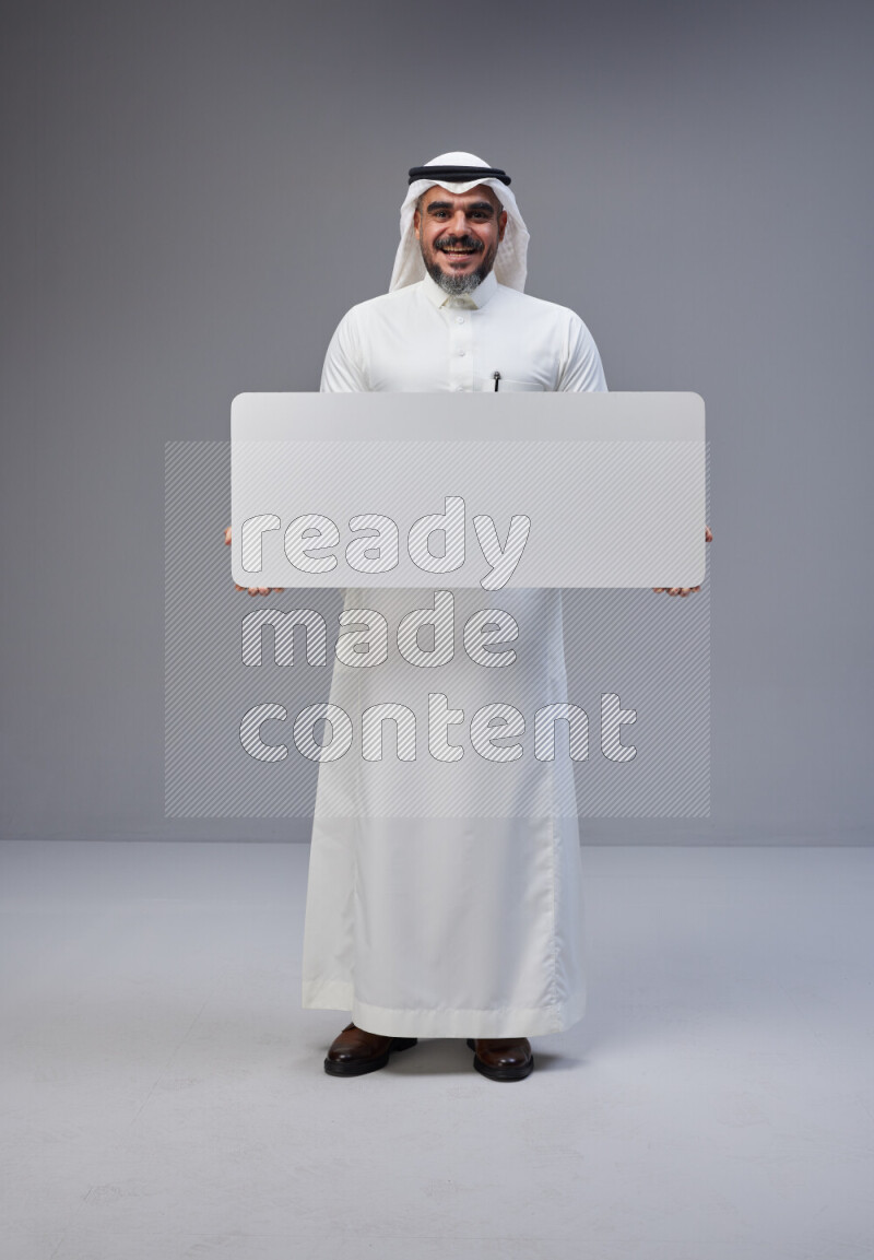 Saudi man Wearing Thob and white Shomag standing holding board on Gray background