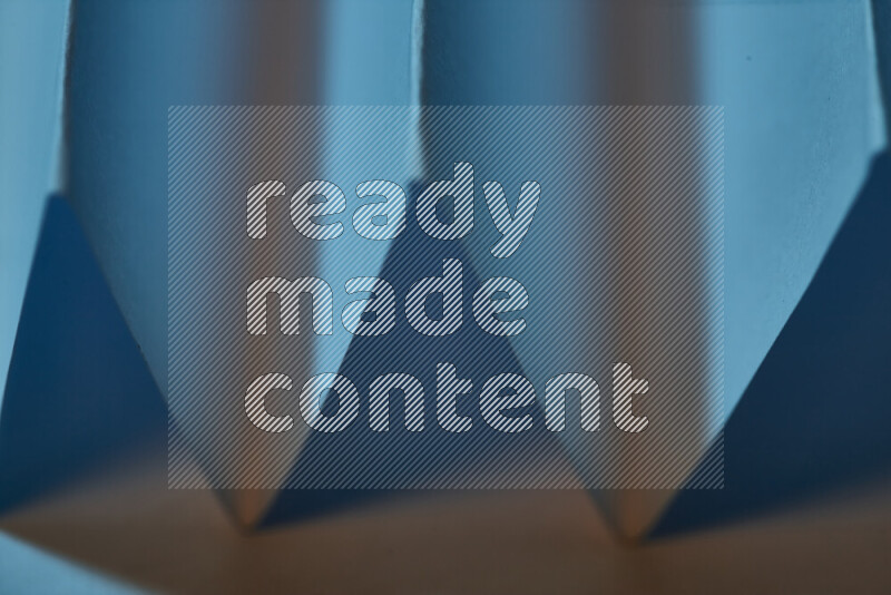 A close-up abstract image showing sharp geometric paper folds in blue gradients and warm tones
