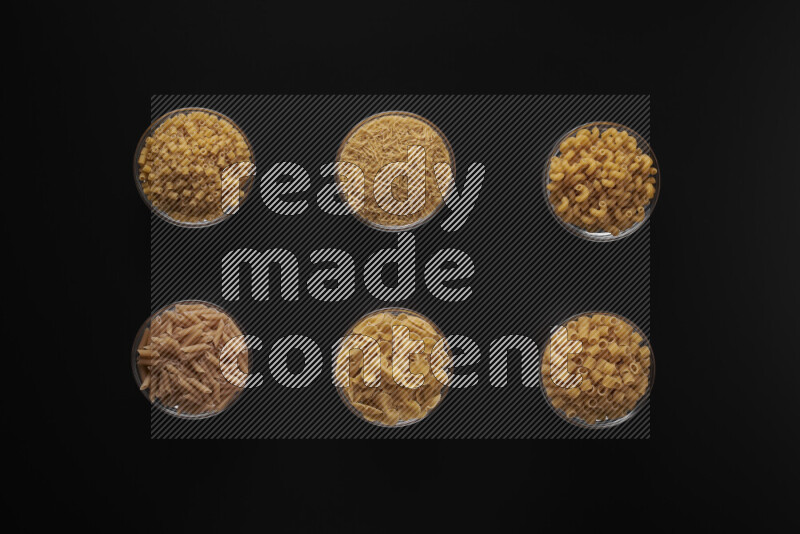 Different pasta types in 6 glass bowls on black background