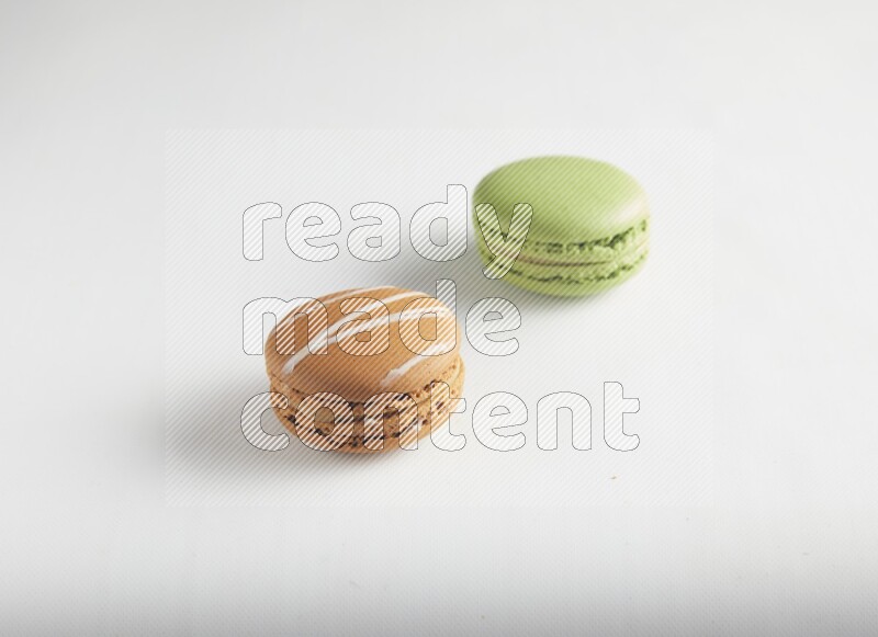 45º Shot of of two assorted Brown Irish Cream, and Green Pistachio macarons on white background