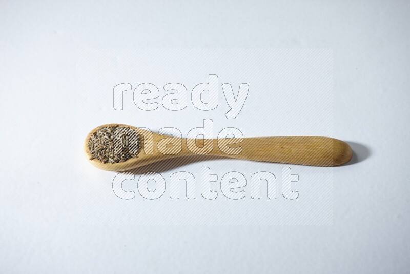 A wooden spoon full of cumin seeds on a white flooring