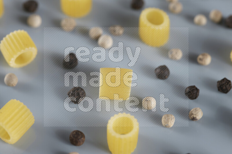 Raw pasta with different ingredients such as cherry tomatoes, garlic, onions, red chilis, black pepper, white pepper, bay laurel leaves, rosemary, cardamom and mushrooms on light blue background