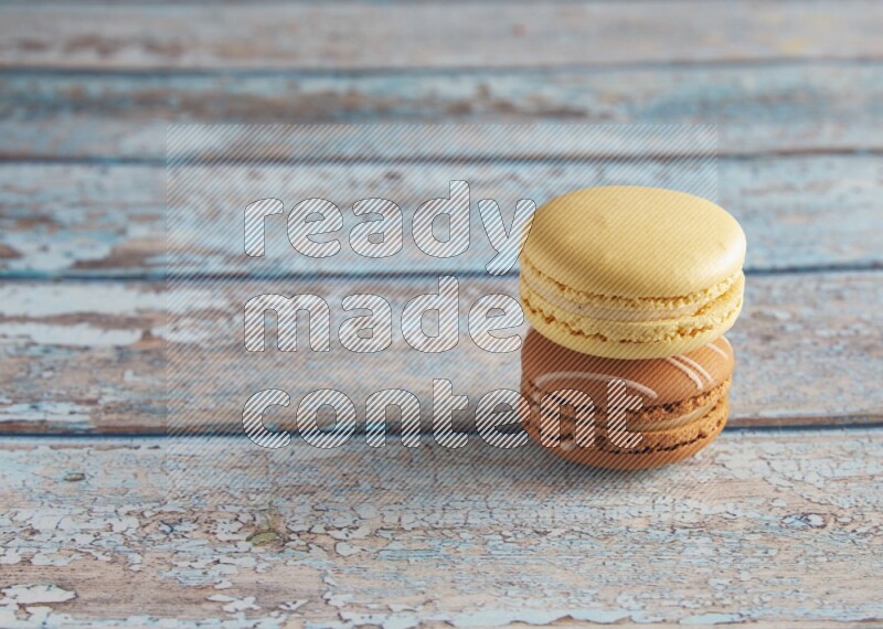 45º Shot of of two assorted Brown Irish Cream, and Yellow Vanilla macarons on light blue background