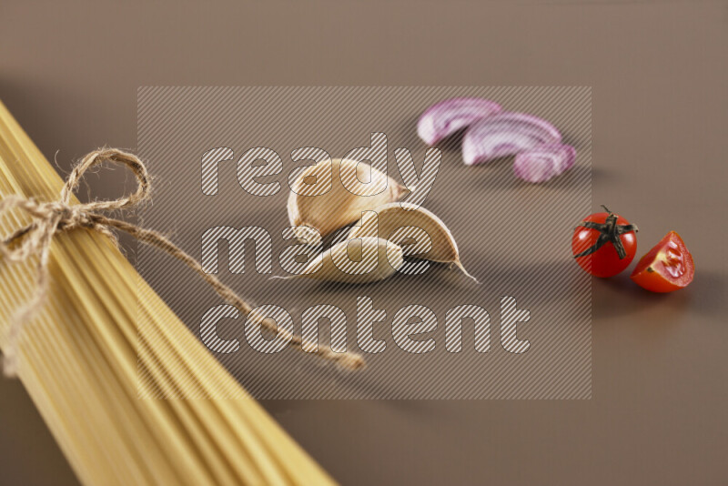 Raw pasta with different ingredients such as cherry tomatoes, garlic, onions, red chilis, black pepper, white pepper, bay laurel leaves, rosemary and cardamom on beige background