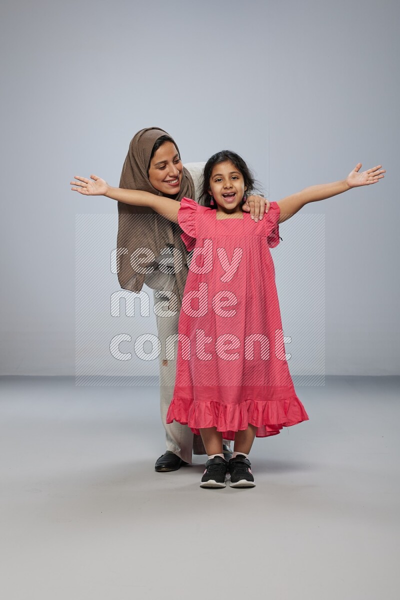 A girl and her mother interacting with the camera on gray background
