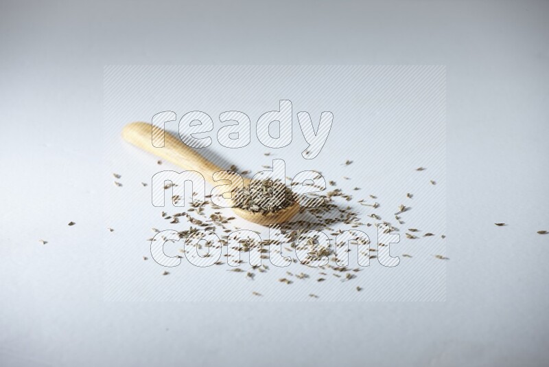 A wooden spoon full of cumin seeds on a white flooring