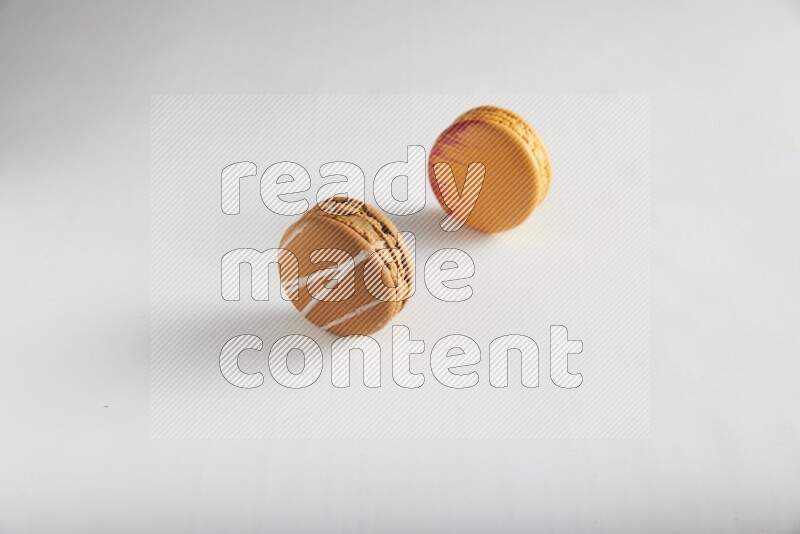 45º Shot of of two assorted Brown Irish Cream, and Orange Exotic macarons on white background