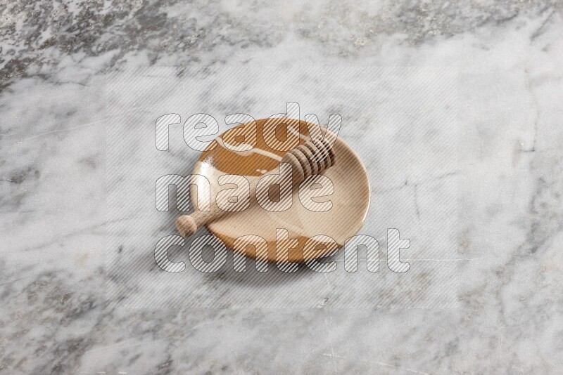 Multicolored pottery plate with wooden honey dipper in it on grey marble background