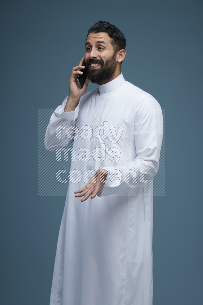 A man having a call on a blue background wearing Saudi Thob