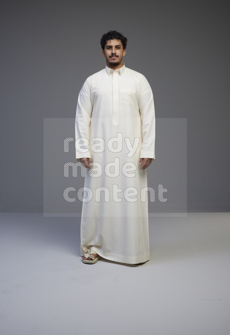 A Saudi man standing wearing thob interacting with the camera on gray background